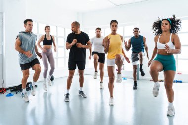 Çok ırklı spor yapan bir grup sporcu, beden eğitimi sınıfında, çok ırklı sporculardan oluşan bir grupta, parlak bir spor salonunda yüksek dizlerini gösteriyorlar.