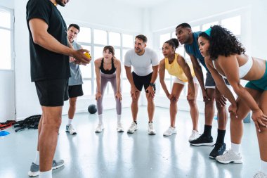 Çok ırklı spor yapan bir grup sporcu, farklı sporculardan oluşan bir spor salonunda egzersiz yapıyor. Eğitmenlerini dinliyorlar. Parlak bir spor salonunda egzersiz yapıyorlar.