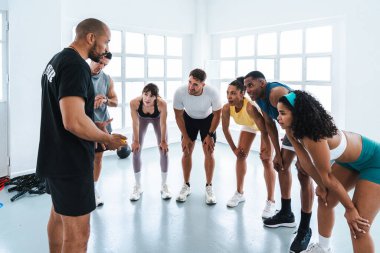 Spor salonunda spor yapan çok ırklı bir grup sporcu antrenörlerini dinleyen bir grup sporcu, parlak ve modern bir spor salonunda egzersiz yaptıklarını anlatıyor.
