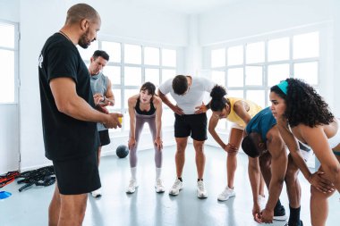 Çok ırklı spor yapan bir grup sporcu, antrenman sınıfındaki yorgun sporculardan oluşan bir grupta antrenörlerinin tavsiyelerini dinlerken nefes alıyorlar. 