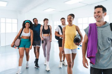 Spor salonunda egzersiz yapan çok ırklı bir grup sporcu çeşitli sporcuların fonksiyonel antrenmanlarını bitirdikten sonra spor salonunu terk etmelerini sağlıyor.