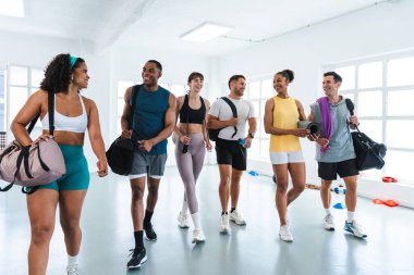 Spor salonunda egzersiz yapan çok ırklı bir grup sporcu, sportif eğitimi bitirdikten sonra spor salonunda yürüyen ve sohbet eden gülümseyen sporcular. Spor çantaları taşıyorum. Yoga paspasları