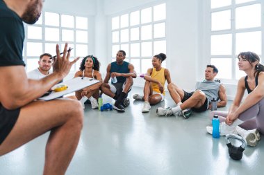 Çok ırklı spor yapan bir grup sporcu, beden eğitimi sınıfında spor yapıyor. Çeşitli sporculardan oluşan bir grup. Kişisel antrenörlerini dinliyorlar. Modern spor salonundaki molada egzersiz rutinlerini anlatıyorlar.