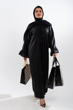 Geleneksel siyah abaya ve tesettür giyen Arap kadın alışveriş torbaları taşırken zarifçe yürüyor, modern tüketim ve kültür zarafetinin bir karışımını sergiliyor.