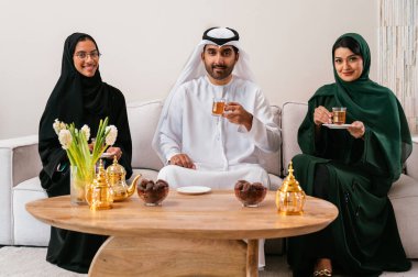 Geleneksel giyinmiş Emirati dostları, modern bir oturma odasında toplanıyor, çay, tarih ve sohbetlerini paylaşıyor, bağlarını ve kültürlerini kutluyorlar.