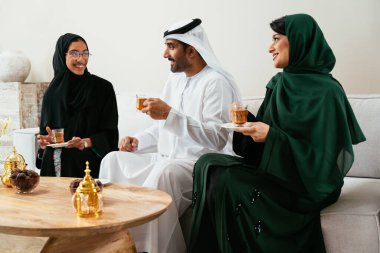 Üç Emirati arkadaşı, iki abayas 'lı kadın ve geleneksel giyimli bir adam, çay içiyor ve karşılama salonunda canlı sohbetler yapıyor.