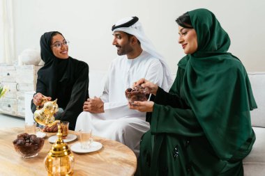Geleneksel abayalar ve kanduralar giymiş Emirati dostları, modern bir oturma odasında buluşmaların, çayın ve sohbetin tadını çıkarıyor, kültürel bağlarını kutluyorlar.