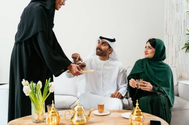 Kız, emirli ailesine geleneksel tatlı ve çay ikram ederek aile bağlarının sıcaklığını ve modern evlerinde kültürel konukseverliğini sergiliyor.