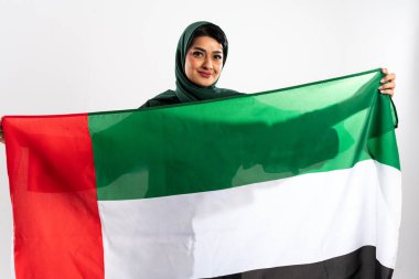 Koyu yeşil tesettürlü Emirati kadını, Orta Doğu 'nun zengin kültürel duvar halısı içindeki ulusal gurur ve kimliği simgeleyen Birleşik Arap Emirlikleri bayrağını gururla taşıyor.