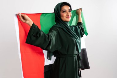 Geleneksel yeşil abaya giyen Emirati kadını ve tesettür gururla bir stüdyo ortamında ulusal gurur, kültür mirası ve vatanseverliği simgeleyen uae bayrağını taşıyor.