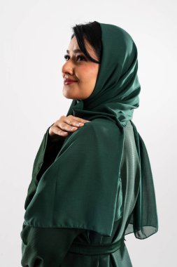 Geleneksel yeşil tesettür ve abaya giyen Arap kadın zarif bir şekilde stüdyoda poz veriyor, özgüven ve kültürel gurur yayıyor aynı zamanda zarafet ve mütevazı modanın vücut bulmuş hali.