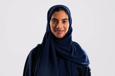 Mavi tesettüre bürünmüş, genç, gülümseyen Müslüman bir kadının portresi, Orta Doğu güzelliğinin, zengin kültürün ve kutsal geleneklerin özünü somutlaştırıyor.