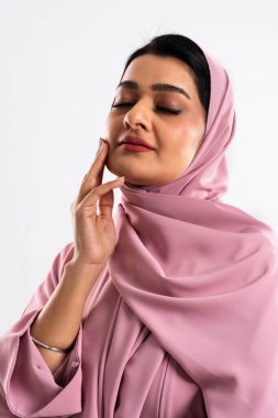 Stüdyo portresi, pembe tesettürlü, genç bir müslüman kadının gözleri kapalıyken yüzüne hafifçe dokunması, dinginlik ve güzellik hissi veriyor.