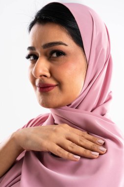 Pembe başörtüsü takmış, geleneksel Müslüman modasını vurgulayan ve kültürel güzelliği zarafet ve özgüvenle kutlayan orta doğulu güzel bir kadının yer aldığı stüdyo portresi.
