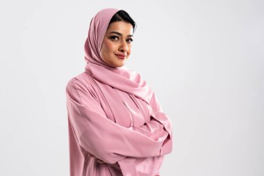 Arap iş kadını, modern Müslüman kadınları iş ve meslek alanlarında temsil eden, şık bir pembe abaya ve tesettüre sahip, bir stüdyo ortamında güven yayıyor.