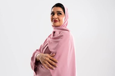 Geleneksel pembe tesettürlü çekici bir Arap kadını gösteren bir stüdyo portresi. Profesyonel bir fotoğraf çekiminde gülümseyen ve kendine güvenen, zarif ve güzel bir poz veren bir kadın.