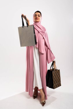 Arap kadın abaya takıyor ve tesettür gururla alışveriş çantalarını profesyonel bir stüdyo ortamında sergiliyor. Orta doğu bağlamında moda, perakende ve tüketimcilik sergiliyor.