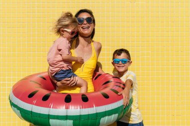 Mutlu güzel Asyalı aile yaz tatilinde kumsalda eğleniyor. Çinli anne ve melez Asyalı çocuklar denizde vakit geçiriyorlar. Aile, annelik ve çeşitlilik kavramları.