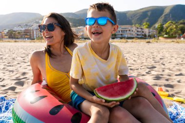Mutlu güzel Asyalı aile yaz tatilinde kumsalda eğleniyor. Çinli anne ve melez Asyalı çocuklar denizde vakit geçiriyorlar. Aile, annelik ve çeşitlilik kavramları.