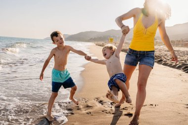 Mutlu güzel Asyalı aile yaz tatilinde kumsalda eğleniyor. Çinli anne ve melez Asyalı çocuklar denizde vakit geçiriyorlar. Aile, annelik ve çeşitlilik kavramları.