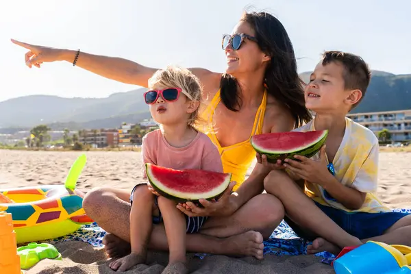 Mutlu güzel Asyalı aile yaz tatilinde kumsalda eğleniyor. Çinli anne ve melez Asyalı çocuklar denizde vakit geçiriyorlar. Aile, annelik ve çeşitlilik kavramları.