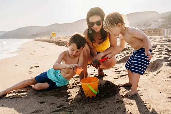 Mutlu güzel Asyalı aile yaz tatilinde kumsalda eğleniyor. Çinli anne ve melez Asyalı çocuklar denizde vakit geçiriyorlar. Aile, annelik ve çeşitlilik kavramları.