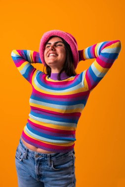 Genç bir kadın kendine has tarzını canlı bir kıyafet ve neşeli bir ifadeyle sergiliyor. Parlak turuncu bir arka plana karşı kendine güveni bireyselliğini ve yaratıcılığını vurguluyor.