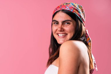Başörtüsü ve omuzunda dövmesi olan neşeli genç bir kadının stüdyo portresi canlı pembe bir arka plana karşı kendine güven ve tarz yayıyor.