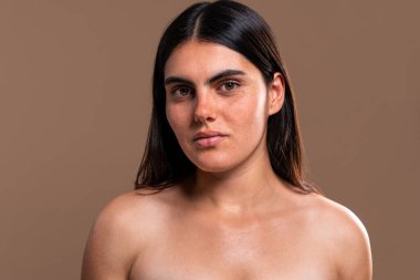 Sakin bir ifadeyle genç bir kadının portresi doğal güzellik ve cilt bakımı sergiliyor. Tarafsız bir stüdyo arkaplanına karşı özgüven ve bireyselliği vurgulamak