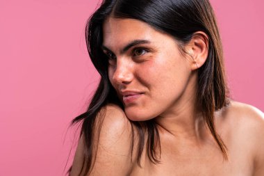 Doğal özellikleri olan güzel genç bir kadın pembe bir arka plana karşı poz veriyor. Cilt bakımı ve kendine özen kavramları somutlaştırıyor. Kendine güveni eşsiz güzelliğini vurguluyor.