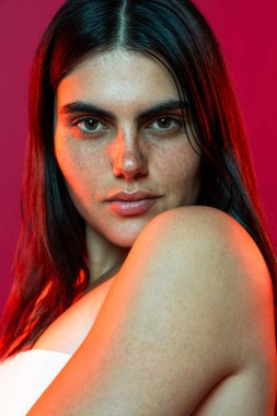 Stüdyo portresi çilli genç bir kadını çekiyor. Omzunda kaotik bir dövme gösteriyor. Çarpıcı kırmızı ışıkla güzelce aydınlatılıyor.