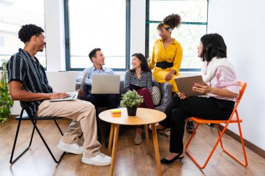 Dizüstü bilgisayarlar ve dijital tabletler kullanarak, çok ırklı iş adamları işbirliği yapıyor, yeni projeleri tartışıyor veya modern ofis alanındaki toplantılarda fikirleri paylaşıyor.