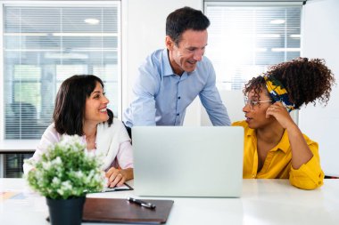 İş arkadaşları takım çalışması yapıyorlar, bir dizüstü bilgisayar kullanıyorlar ve fikirleri tartışıyorlar, dinamik bir ofis ortamında işbirliği ve yeniliği teşvik ediyorlar