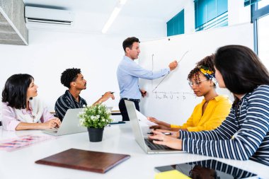 Çağdaş bir ofiste işbirliği yapan çeşitli iş adamları, verimli bir toplantı sırasında beyaz tahtada sunulan büyüme grafiklerini ve mali verileri analiz ediyorlar.