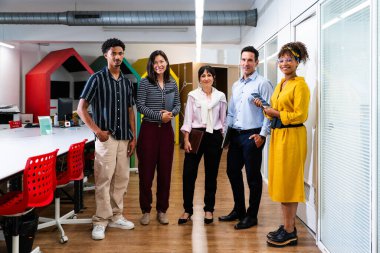 Modern ofis koridorunda takım çalışmasını, çeşitliliği ve başlangıç ortamında işbirliğini temsil eden çok ırklı iş adamları bir arada duruyor.