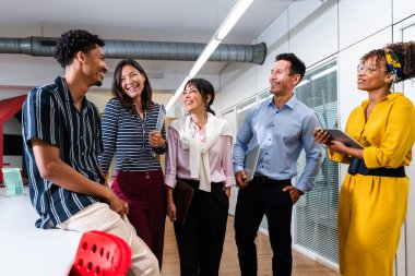 Modern bir ofiste birlikte çalışırken gülümseyen ve fikirleri paylaşan çok ırklı iş adamları, başlangıçtaki ortamlarında işbirliği ve yeniliği teşvik ediyorlar.