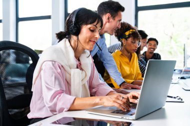 Modern ofis ortamında iş birliği ve problem çözme ekibi, kulaklıklı bir dizüstü bilgisayar kullanarak müşteri hizmetleri temsilcisine odaklanıyor.