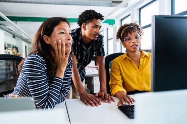 Çağdaş bir ofis ortamında bir masaüstü bilgisayarının etrafında toplanmış, verileri analiz ediyor ve iş dünyasının başarısı için strateji oluşturuyorlar.