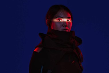 Stüdyoda duran bir kadın, yüzü kısmen gözlerindeki kırmızı ışık tarafından aydınlatılmış, mavi ve mor gradyan arkaplanda dramatik ve gizemli bir siber punk atmosferi yaratıyor.