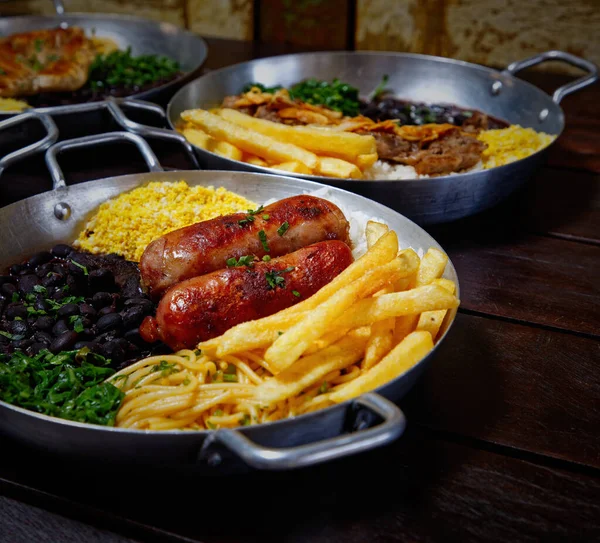 Tahta bir masada patates kızartması ve siyah bir tavada farklı tabakların yakın plan fotoğrafı.