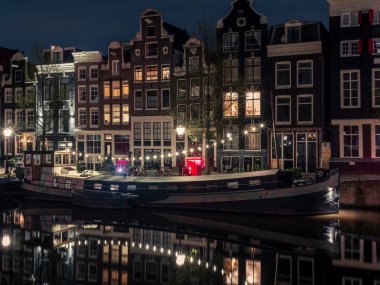 Aydınlatılmış bir yüzen ev, Amsterdam 'daki Singel Kanalı' na gece yansıyor.