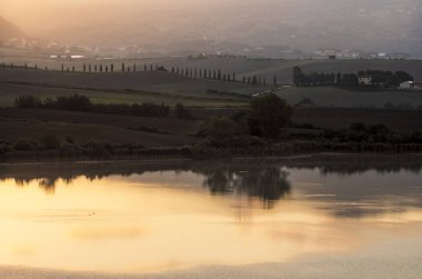 Tuscan kırsalındaki Santa Luce Gölü, tipik tepe ve ağaç manzarası ile renkli bir gündoğumu sırasında
