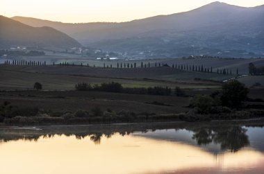 Tuscan kırsalındaki Santa Luce Gölü, tipik tepe ve ağaç manzarası ile renkli bir gündoğumu sırasında