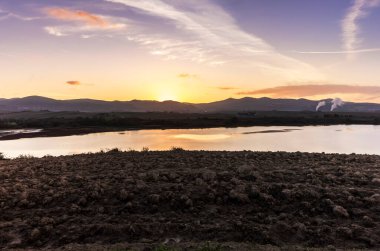 Tuscan kırsalındaki Santa Luce Gölü, tipik tepe ve ağaç manzarası ile renkli bir gündoğumu sırasında