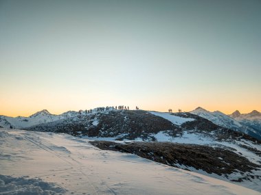 Erken saatlerde İsviçre 'deki Lenzerheide Staetzerhorn tepesinden Alp Dağları' nda renkli bir güneşin doğuşunu izleyen insanların siluetleri.