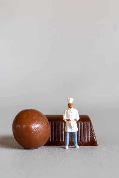 灰色の背景を背景に立ちながら チョコレートスタンディングを持つミニチュアの人々のシェフ — ストック写真
