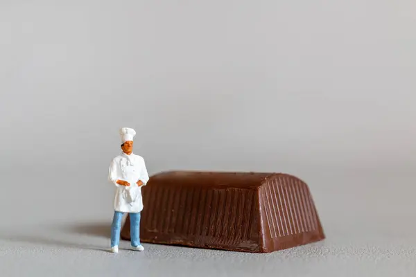灰色の背景を背景に立ちながら チョコレートスタンディングを持つミニチュアの人々のシェフ — ストック写真