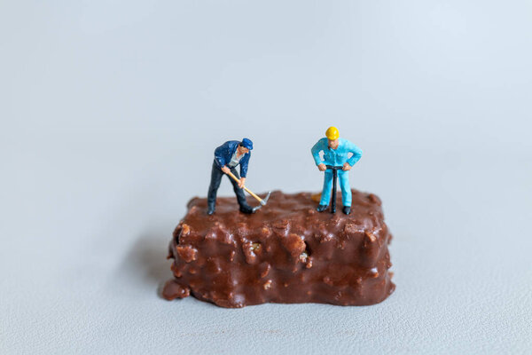 Miniature people , An employee is making a chocolate bars on gray background. World Chocolate Day Concept