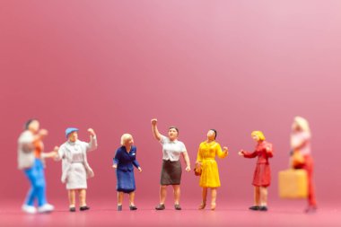 Minyatür insanlar, bir grup kadın, Uluslararası Kadınlar Günü 'nün pembe arka planında bir araya gelirler.