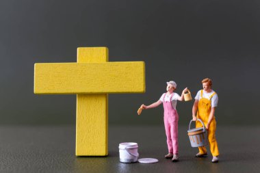 Minyatür insanlar, bir sanatçı tarafından yapılmış sarı bir haç, Good Friday konsepti.